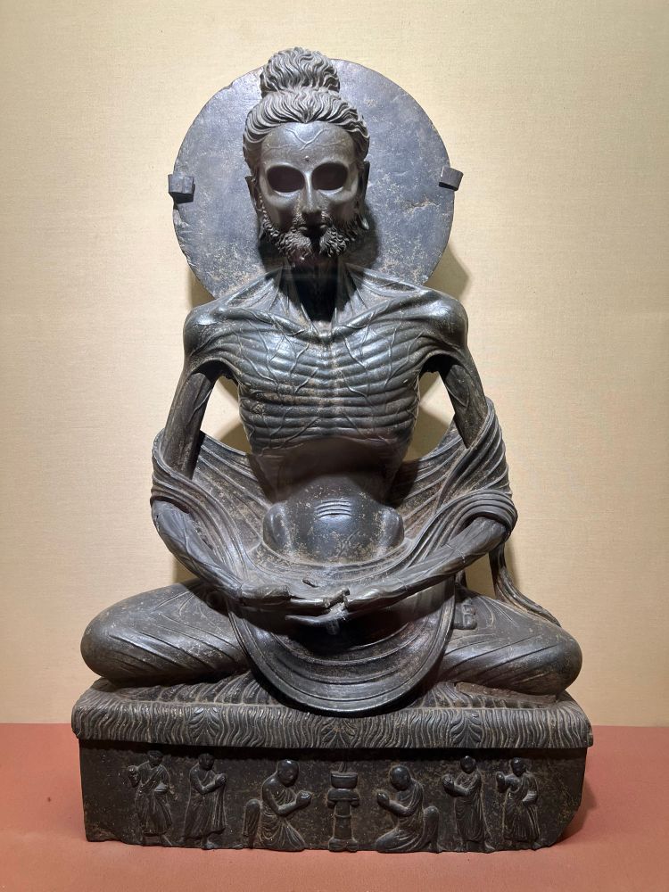 Dark stone statue of an emaciated Buddha in meditation posture