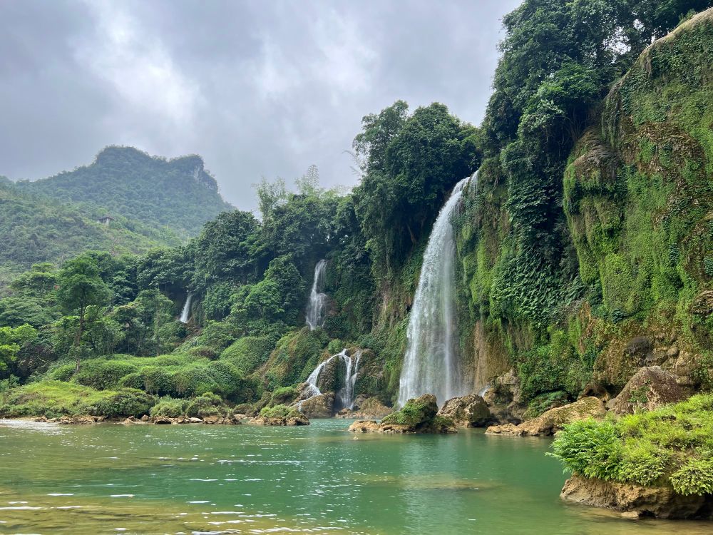 Waterfall from green cliffs with aquamarine pool in foreground and green hills in backfield
