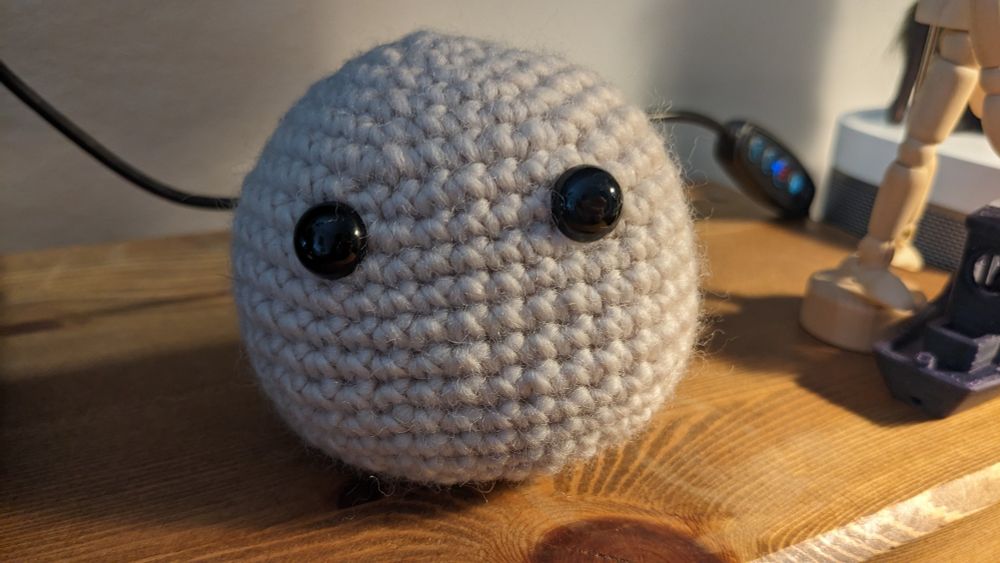 A small crochet ball in a light cream colour, with a set of doll eyes.