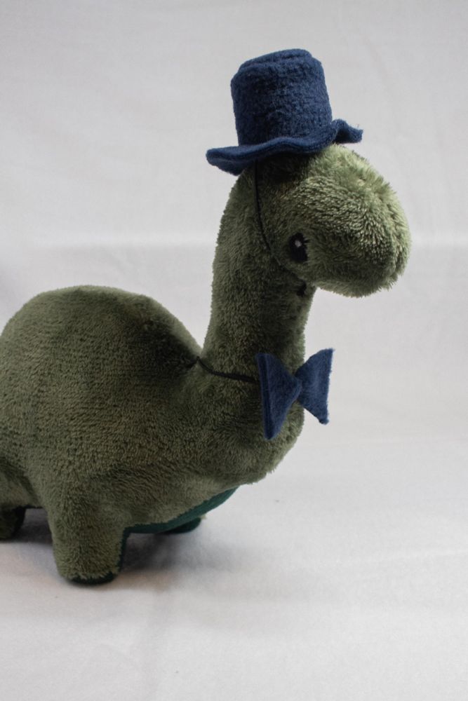 Green Brontosaurus plush wearing a top hat and bowtie facing right with a white background 