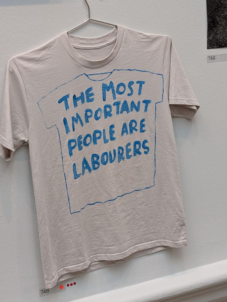 A white t-shirt on a hanger, with a text on it (in blue) saying "The most important people are labourers"