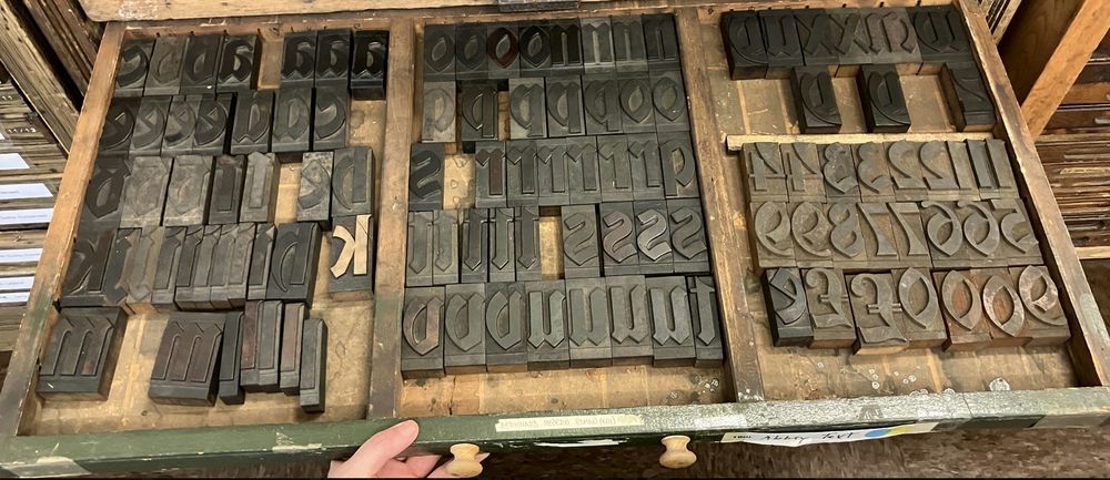 Photo of a letterpress typecase (wide, shallow drawer) pulled out from its cabinet to show the 2" tall wooden letters (in a medieval typeface called "Abbey Text") it organizes