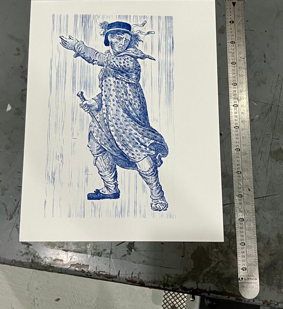 Photo of a letterpress print on different white paper with navy blue ink, showing a 9" tall image from a historical painting of a "Luddite General", a man in a 19th-century dress beckoning onward, surrounded by a light background of vertical wood grain lines. 