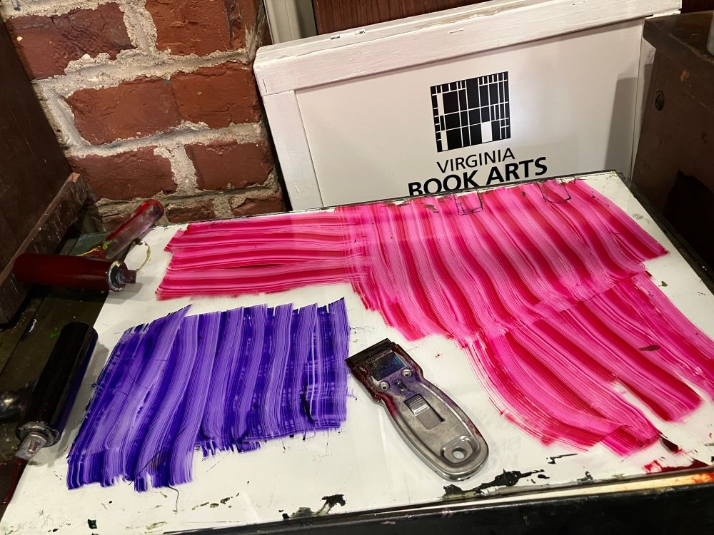 Photo of a glass inking plate that's had people and magenta ink on it, now mostly scraped away using a straight razor leaving a lined pattern of ink