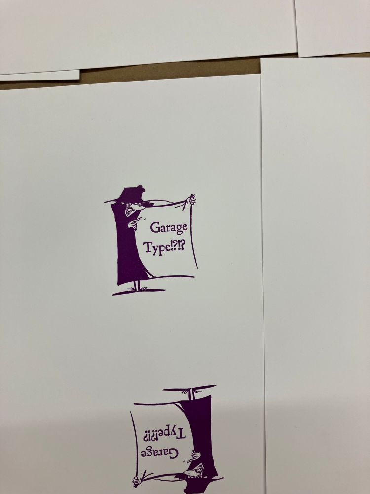 Photo of a piece of white paper in which the same design has been printed twice, the second time 180 degrees reversed. The design is printed in dark purple ink and shows a cartoon of a shifty person trying to sell you something from inside one side of an opened trechcoat; inside the trenchcoat is printed the text "Garage type!?!?"