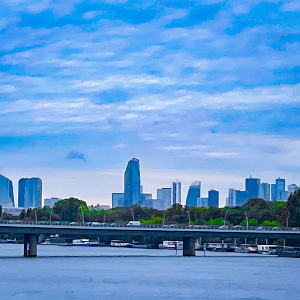 Le quartier de La Défense vu du pont de Saint Cloud, sous fond de ciel nuageux mais bleu quand même par la magie de photoshop, au premier plan l’autoroute de Normandie passe au-dessus de la Seine où coulent nos amours, et entre lesdits pont et quartier se distingue le bois de Boulogne 