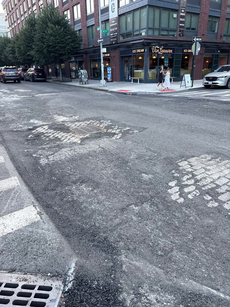 A street in Brooklyn being replaced. A series of Belgian blocks can be seen peaking out beneath the asphalt 