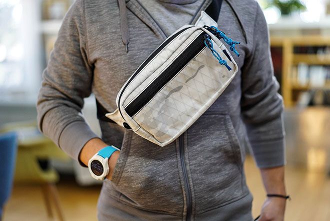A photo of a man wearing a gray cross body bag over a hoodie. 