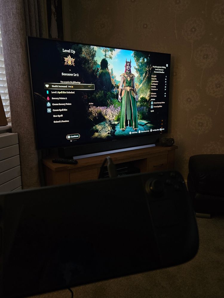 Baldur's Gate 3 playing on the telly in the living room, powered by my Steam Deck which I'm holding up.

It's on the level up screen, and I'm choosing options for my Mephistopheles Tiefling Draconic Bloodline sorcerer