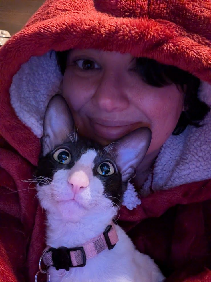 a person and a black and white cornish rex cat, smiling together for a picture