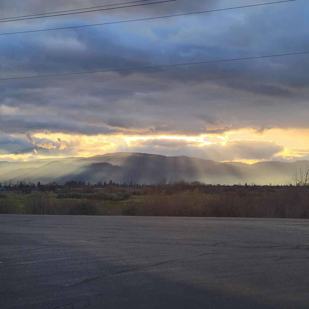 Sunset over mountain; overcast sky is casting pillars of light over a foggy sparse landscape