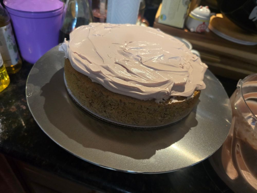 A banana cake on a turntable with whipped cream spread on top