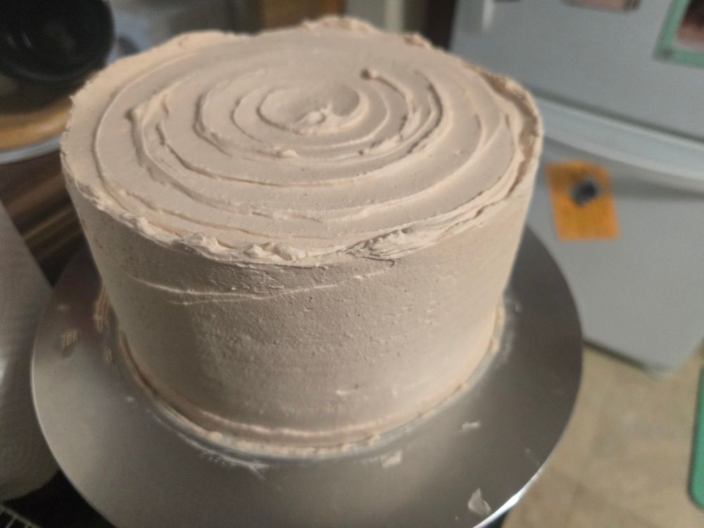 The previous cake, fully covered in whipped cream, with a spiral pattern on the top