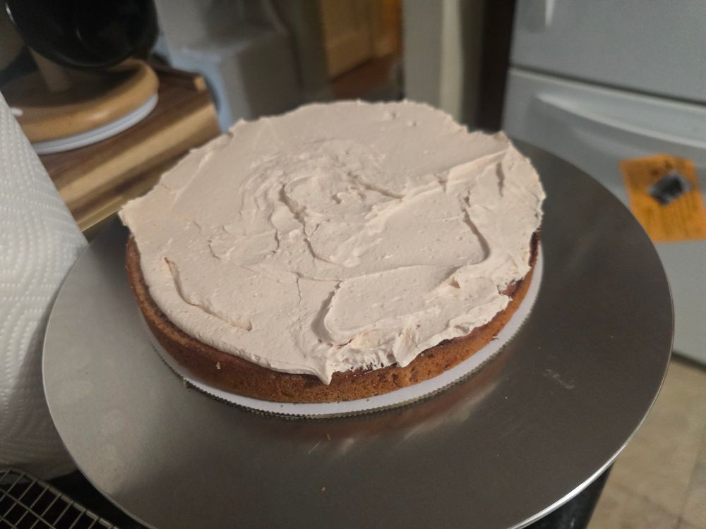 A cake on a turntable with whipped cream spread on top
