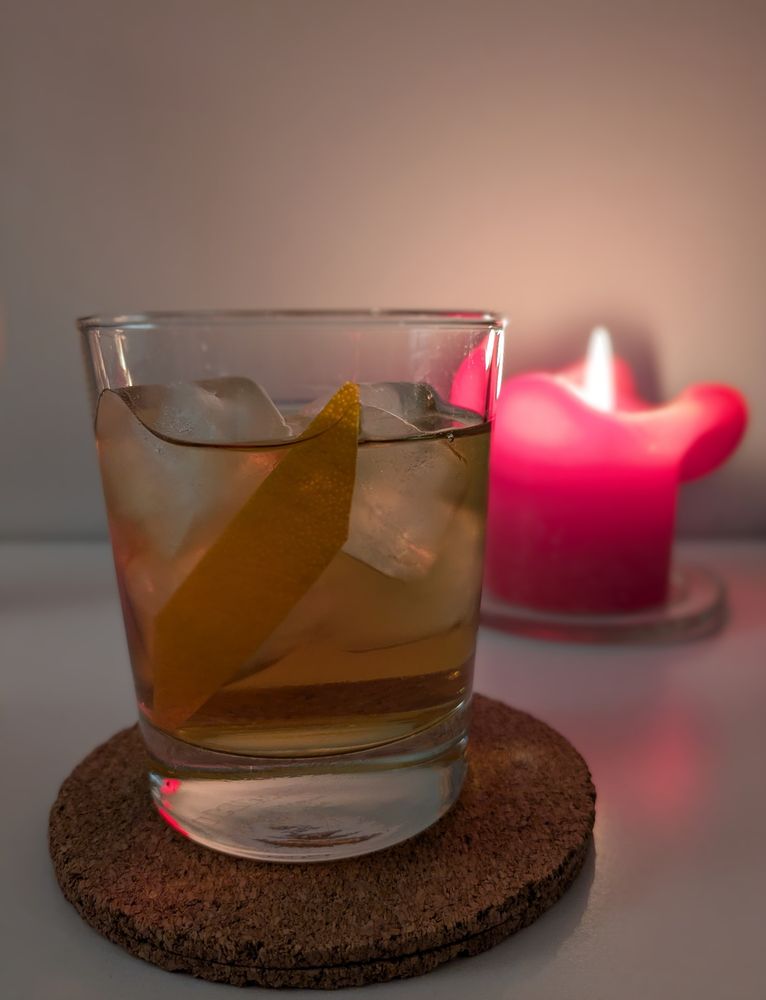 A cocktail in a rocks glass, with a lit candle behind it, trying to be artsy but ending up quite a mundane photo... But the drink is good!