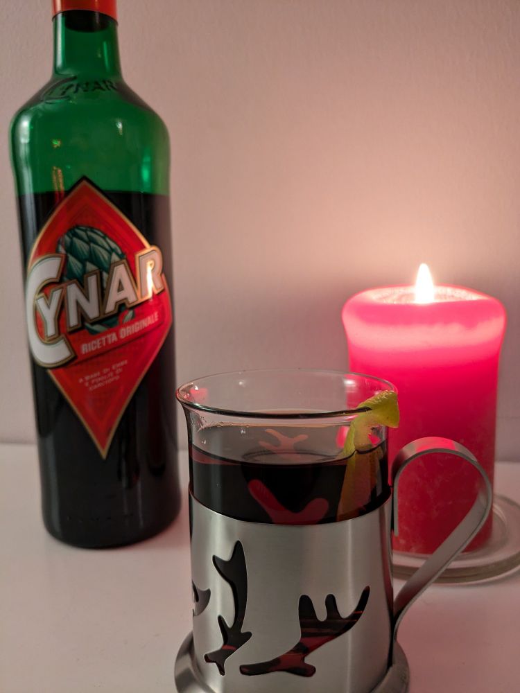 A glass of Amaro Caldo made with Cynar, a bottle of Cynar, and a lit candle