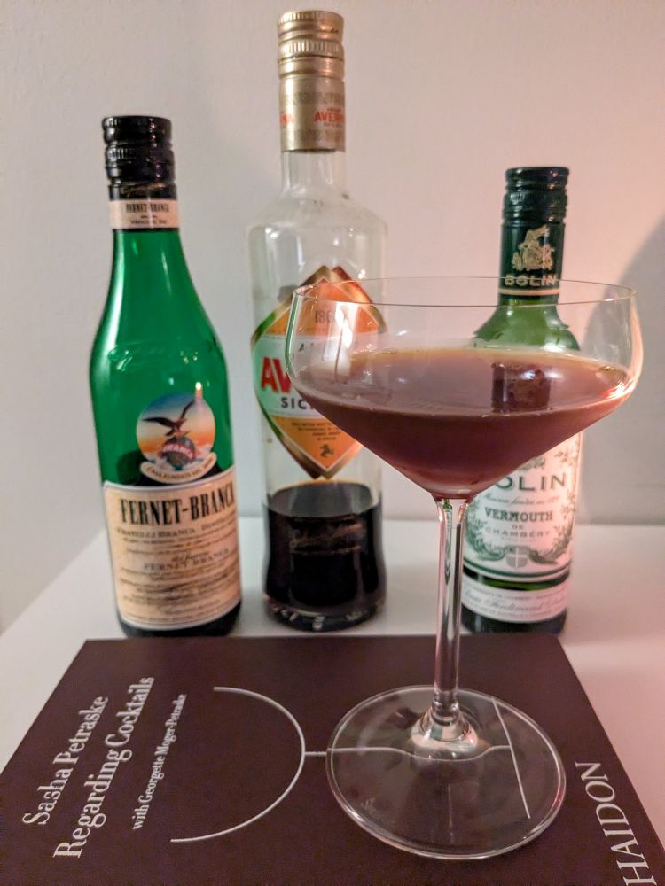A San Francisco Treat cocktail in a coupe glass, with bottles of Averna, Fernet-Branca, and Dolin Dry - its ingredients.