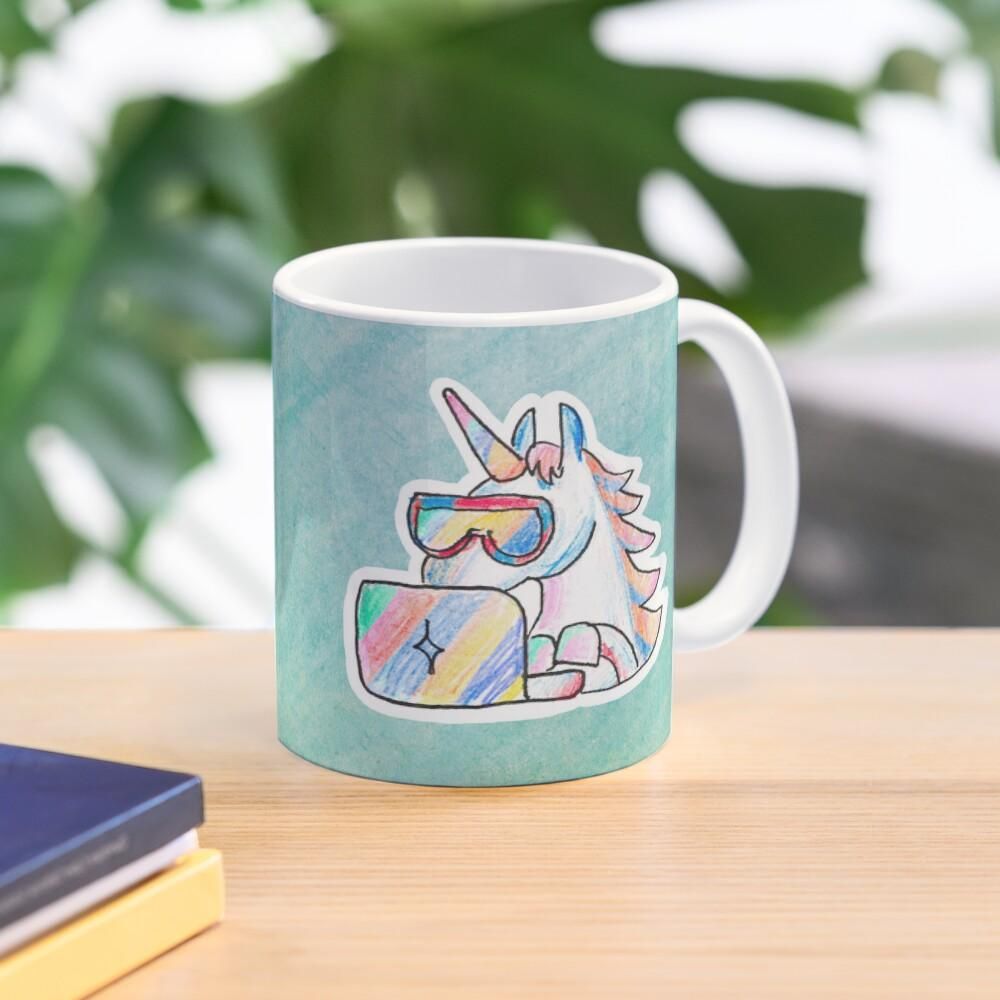 Product photo of a mug with a colorful hand-drawn unicorn wearing cool googles and typing into a notebook. The background of the artwork is greenish.