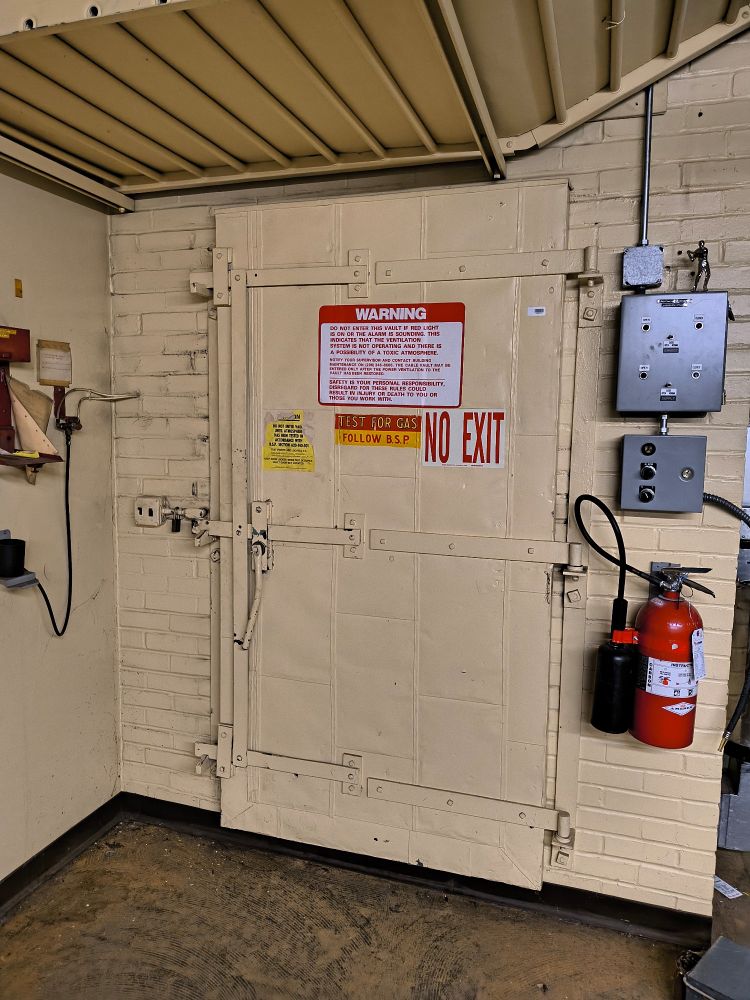 Large steel door with several warning signs and a control panel