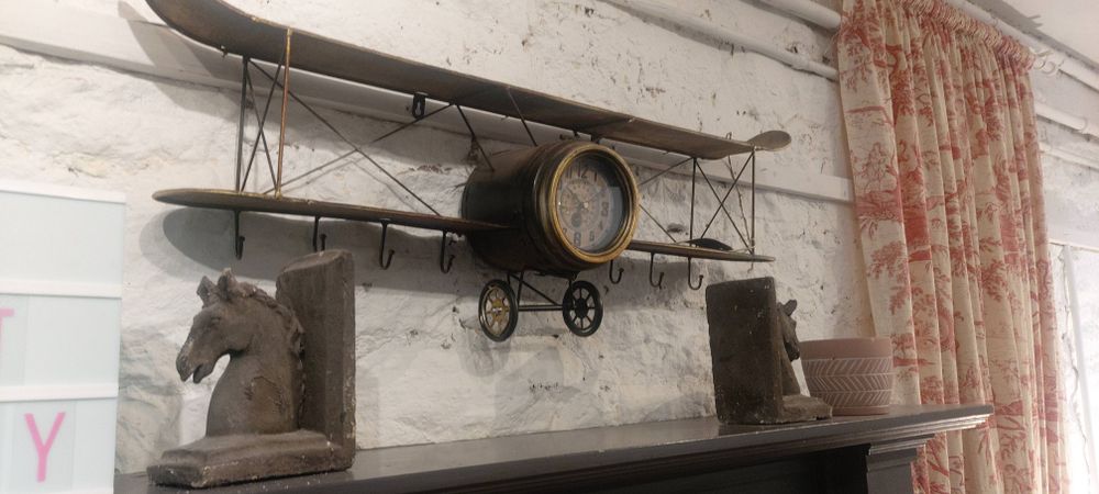A model aeroplane on a stone wall above a mantlepiece, with horse-shaped bookends resting on the mantle. The nose of the plane is replaced by a clock.