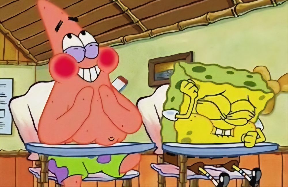 A photo from a SpongeBob episode when SpongeBob and Patrick are joking about "what's funnier than 24?". SpongeBob is sitting to the right, and Patrick is sitting to the left. They are both sitting in seashell shaped desks in a classroom. Patrick has red cheeks and a smile on his face. He’s holding his hands up to his mouth. SpongeBob is hunched over with his left fist on the desk and right fist over his head. His eyes and mouth are closed, with his two front teeth coming out over his bottom lip. SpongeBob is trying not to laugh.