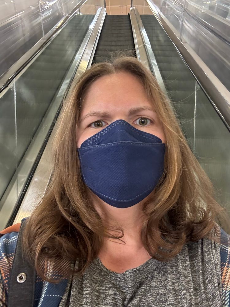 A woman wearing a navy KN94 mask with light brunette hair that have massive curls at the ends.
