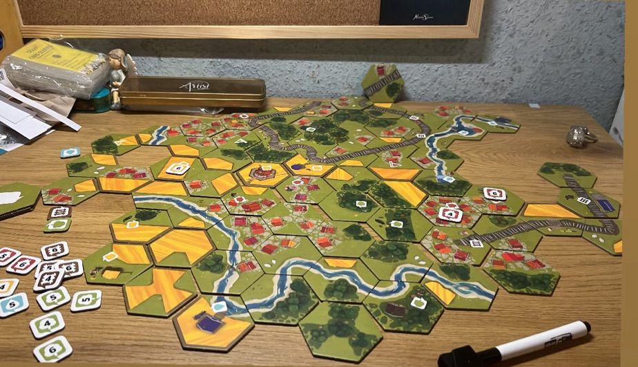 chaotic desk with a game called dorfromantik spread across