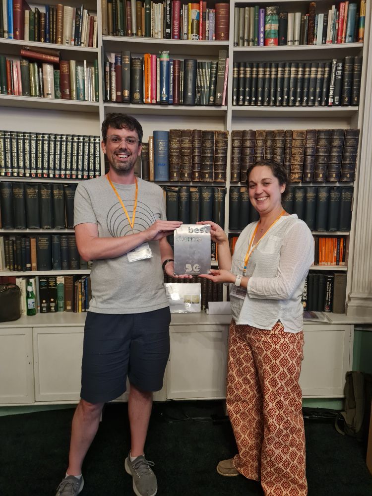 A white man and white woman hold a silver trophy in front of a book case