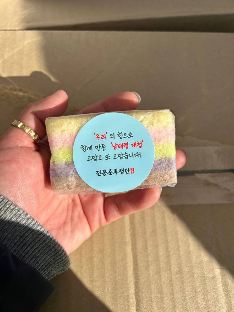 白ピンク緑紫グレーのストライプのお菓子を持っているでの写真｡ハングルのメッセージシールが貼ってある