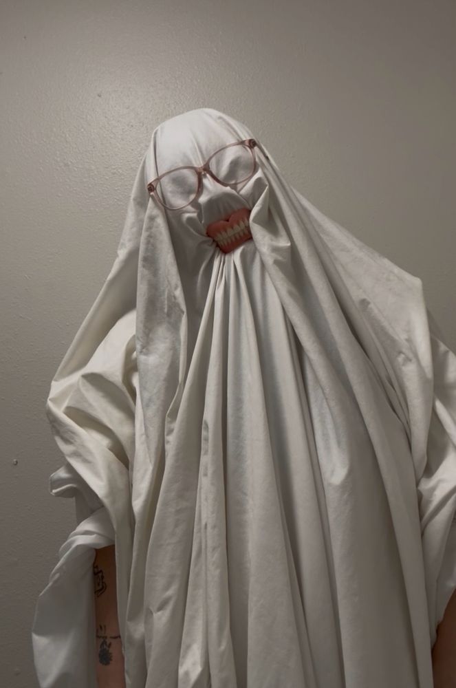 I am pretending to be a ghost with teeth and glasses. I am in a white sheet with glasses and dentures. 