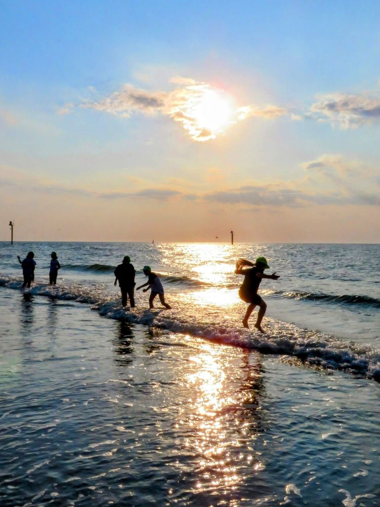 Silhouetten von im Meer spielenden Kindern, im Gegenlicht der Sonne.