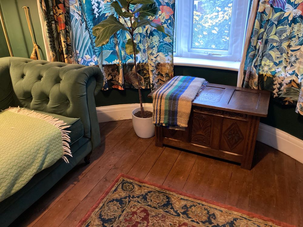 A blanket box covered with a blanket, next to a green sofa