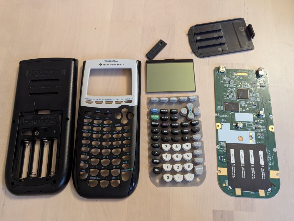 The parts of the TI-84 Plus calculator have been disassembled and are ready to attach to the backdrop. From left to right is the back case of the calculator, the front case of the calculator, the screen and keypad, the PCB, and the battery cover and smaller backup battery cover.