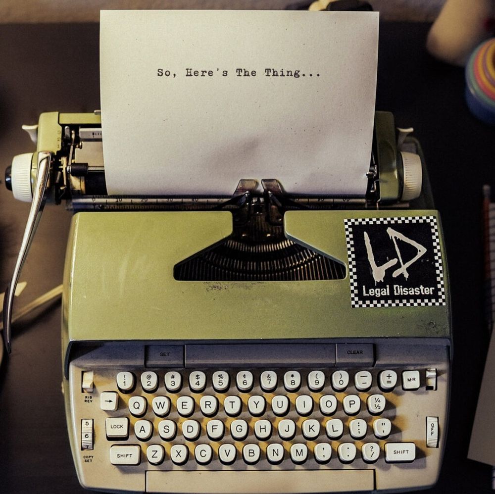 Album cover art is a photo of an old school typewriter with a Legal Disaster sticker on it. The paper coming out of the topnof the typewriter has the album title typed across the top "So, here's the thing..."