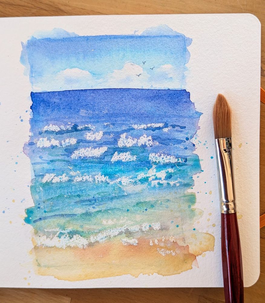 Watercolor sketch from my sketchbook of ocean waves under a blue sky on a sandy beach, sketchbook page and a paintbrush, by Karen Kaspar