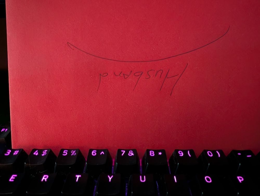 A red envelope with the word "husband" on it, placed upside down on the  keyboard of my desktop computer. 