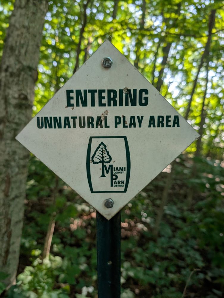 A park sign that says "Entering Unnatural Play Area" 