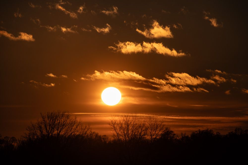 The sun hangs above the horizon, glowing, clouds above giving it an eyebrow
