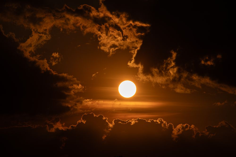 A glowing orb surrounded by dark clouds in a russet sky. 