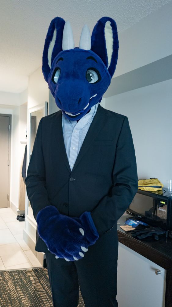 Adelair, a purple dragon fursuiter, appears wearing a grey suit and shirt