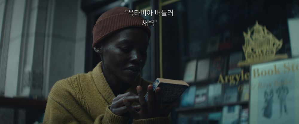 Lupita Nyong'o, dans A quiet place : Day one, lit la quatrième de couverture de L'aube de Olivia E. Butler