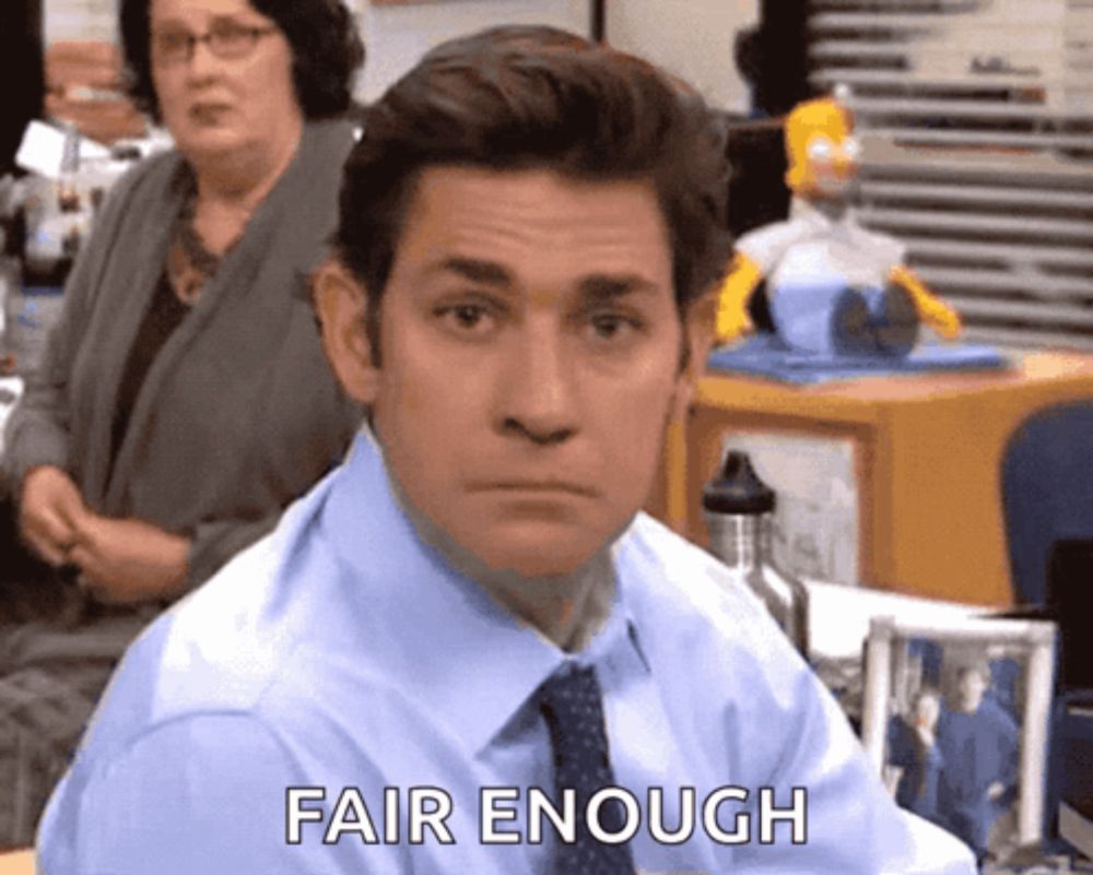 a man in a blue shirt and tie is sitting at a desk and saying fair enough