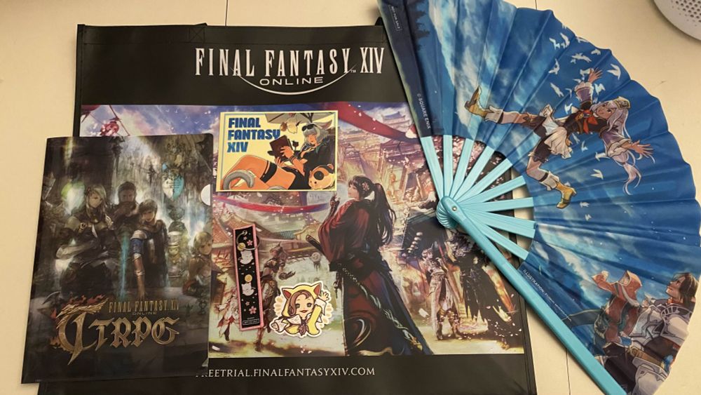 Freebies from completing their stamp rally at the FFXIV booth. Contains a large rectangle-shaped plastic bag with an art of a female Hyur Samurai in Kugane, a large fan containing art of Prishe and other adventurers, a trial booklet of the FFXIV TTRPG, sticker of the Y'shtola in summer glam art, a pink border tag with moogles, and a Krile sticker.
