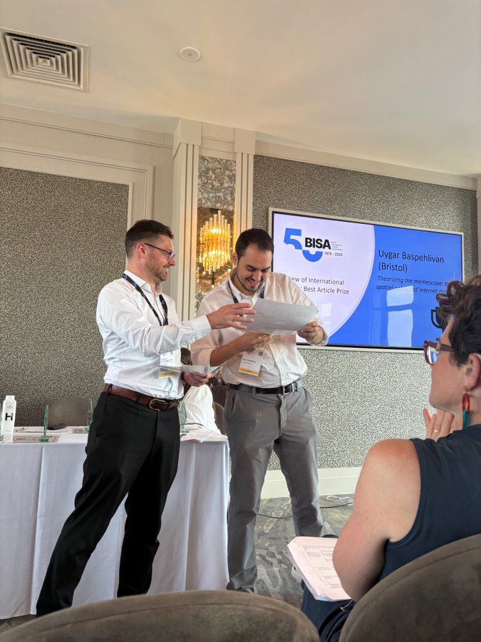 Uygar collecting his award given to him by editor of the RIS. In the background there is a BISA powerpoint slide with details of the prize. 