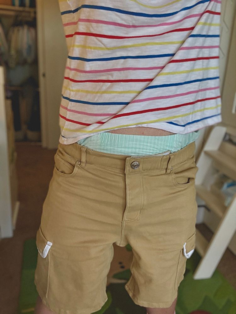 Abdl boy in cargo shorts and a striped shirt with a diaper peeking out obviously above his waistline.