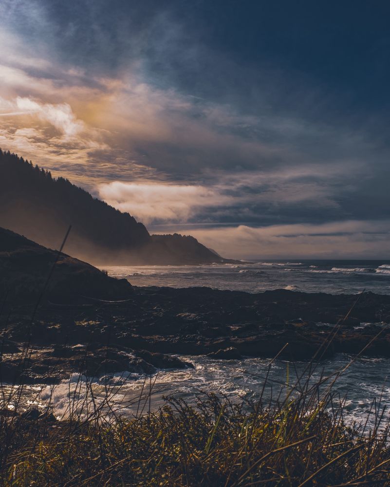 A color film photograph taken in Florence, Oregon of the Cape Perpetua peninsula from afar. A marine layer moves in as the evening sun starts to set over the Pacific.