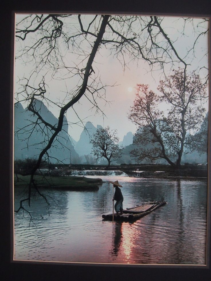 A man paddles a small flat craft against a backdrop of jagged mountains.