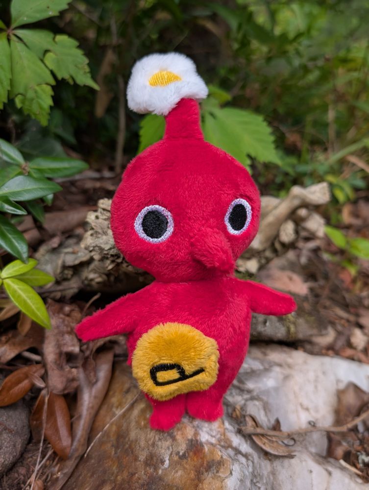A handmade Red Pikmin plushie with a magnetic P sticker on its body.