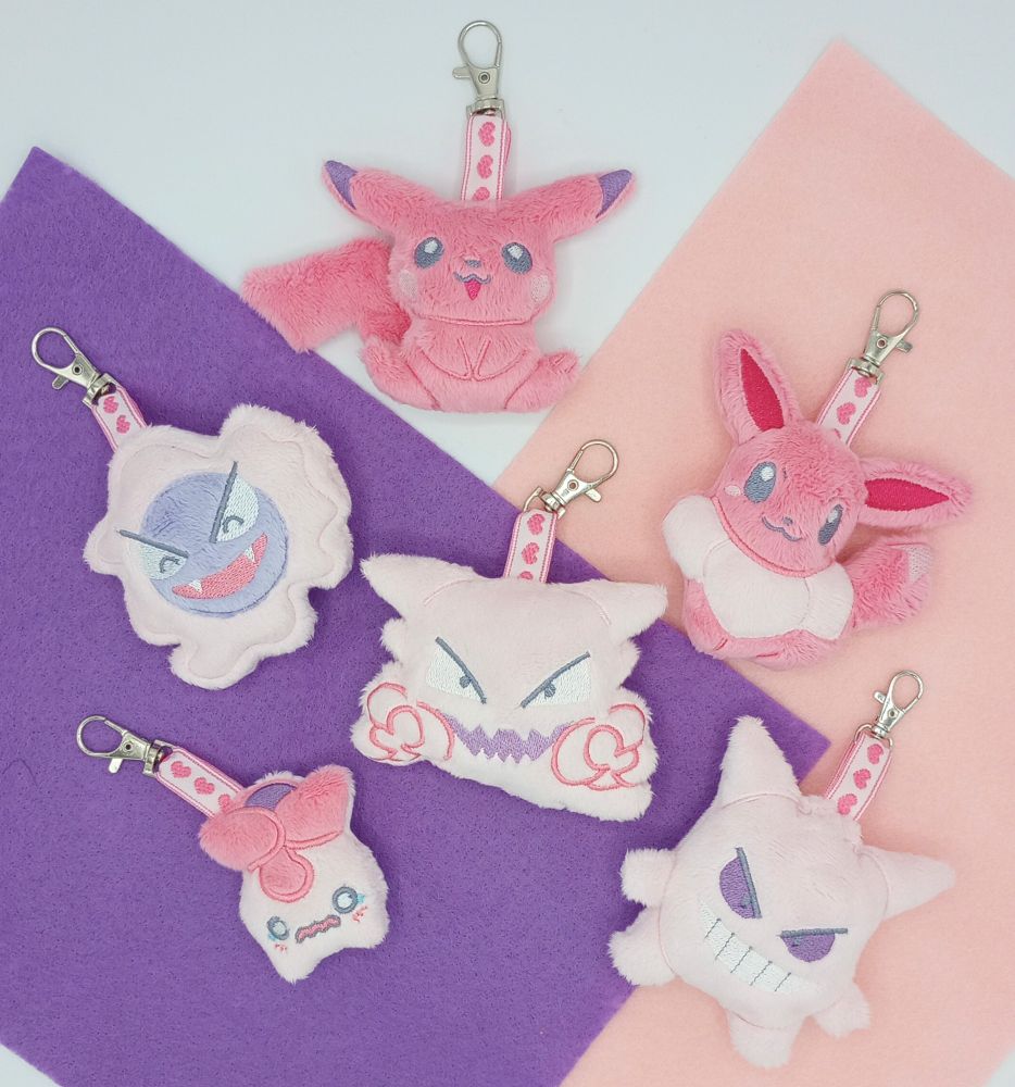 A collection of handmade pink Pokemon plush keychains.  From top to bottom: Pikachu, Gastly, Eevee, Haunter, Smoliv, and Gengar.