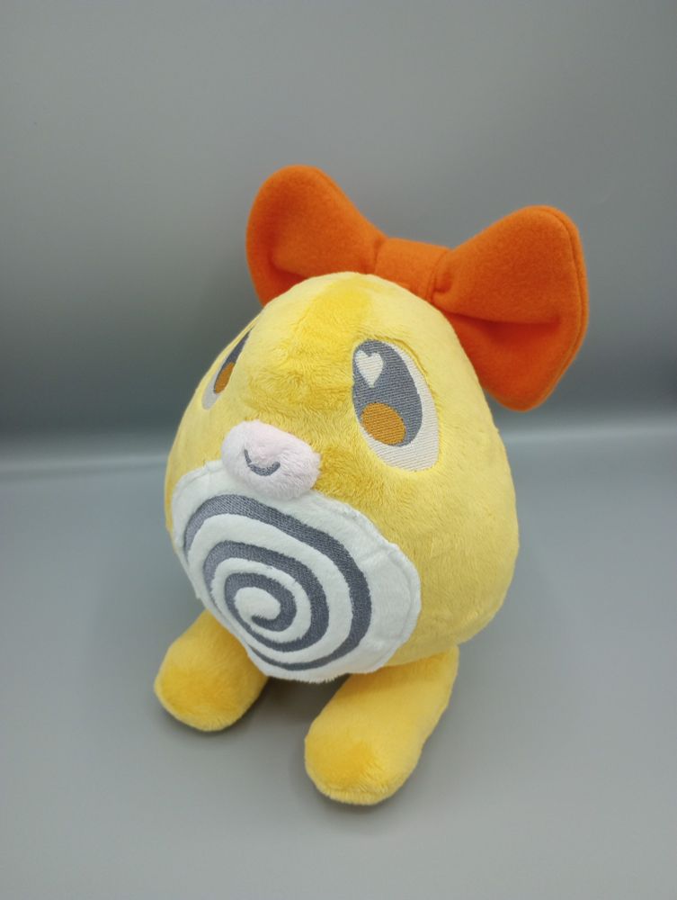 A handmade yellow Poliwag plushie from Pokemon.  It has a large orange bow on its head.